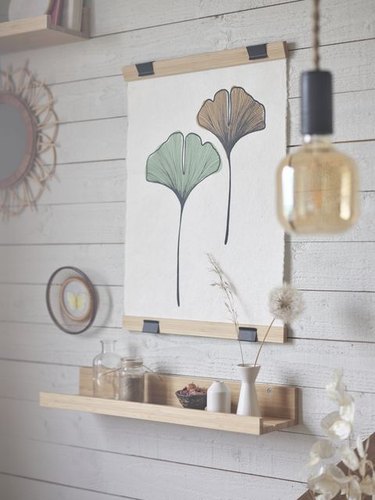 Two flowers on a poster, one green and one red. The poster is hanging on a wooden wall above a wooden shelf with trinkets on it