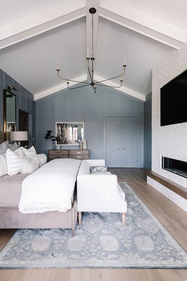Bedroom with vaulted ceilings, blue accent wall and neutral bedding.