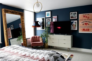 Cozy bedroom with dark navy blue walls and tall standing gold mirror.