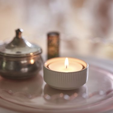 A white candle holder with a lit candle on a plate