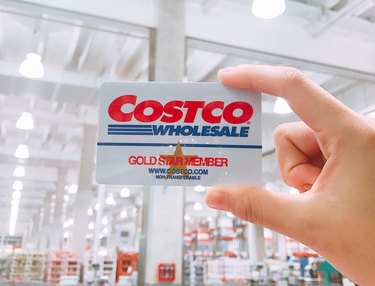 A hand holding up a Costco Gold Star Member card in a Costco warehouse.