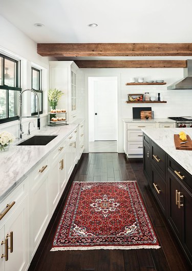 Black and white kitchen with warm red rug and dark wood beams