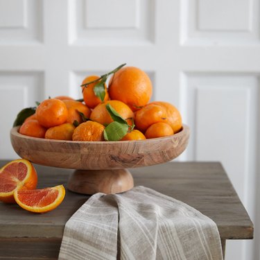 table with wood serving bowl filled with oranges