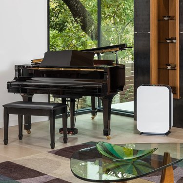 A white air purifier in a room next to a black piano