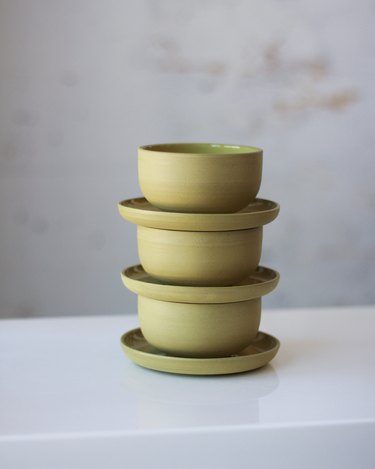 Three green cups with saucers stacked on top of each other in front of a gray background