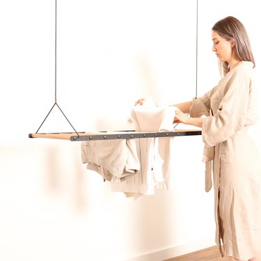 Woman putting white clothes on a drying rack that is hanging from the ceiling
