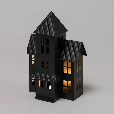 A black haunted house sculpture with lit fake white candles inside that give off a cozy glow through the windows.