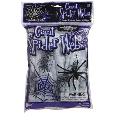 A clear package of white spiderwebs with small black fake spiders in it. The package says "Giant Spider Webs" in a purple and white font.