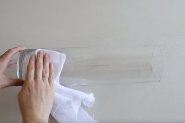 Wiping long cylindrical glass vase with a cleaning cloth