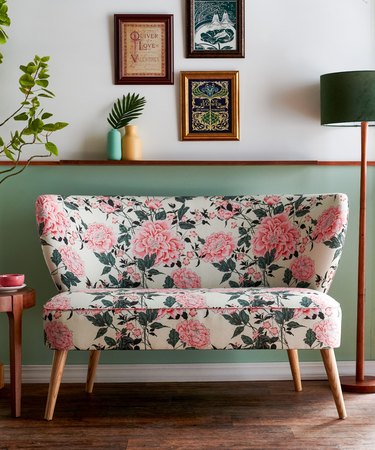 floral loveseat near white and green wall with floor lamp and framed art