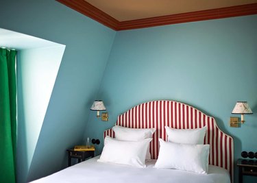 Blue bedroom with red headboard and green curtains.