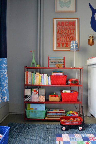 Little boys room with gray walls, navy curtains, and red artwork and shelving.