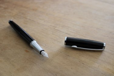 A ball fountain pen with the cap off on a light wood surface.