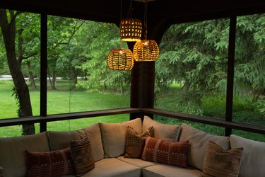 A trio of basket pendant lights over a sectional sofa with a view of a forest landscape