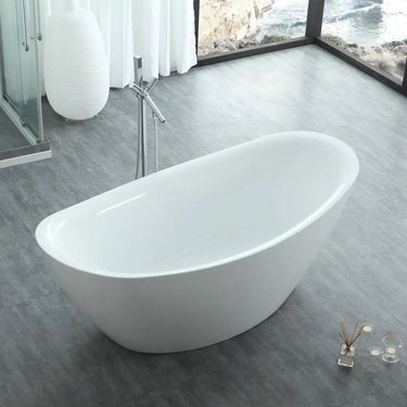 An acrylic white bathtub in a bathroom with glass exterior doors and grayish wood floors