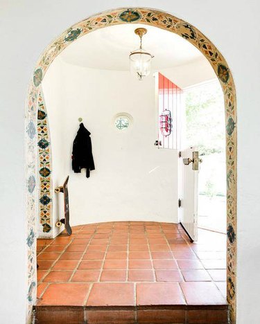A white entryway with Saltillo tile and a yellow tiled arch.