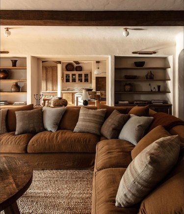 Brown living room with cozy caramel sectional and round dark wood coffee table.