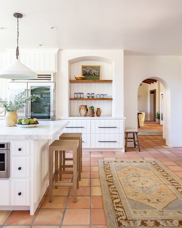 White kitchen with tan barstools, neutral rug, and Saltillo floors.