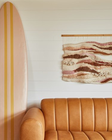 Closeup of a portion of the Lobby Bar of the June Motel with caramel leather sofa, boho wall hanging and blush and mustard surfboard.