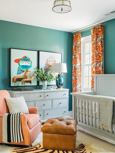 Nursery with light gray furniture, teal walls, and orange curtains