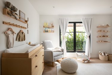 Another view of the Scandinavian nursery with a close-up shot on the wood changing table and a large window with greenery peaking through in the background.