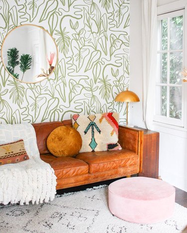 Airy living room with caramel leather sofa, green and white wallpaper, and pink pouf.