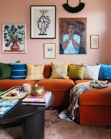 Blush-walled room with orangey caramel velvet sofa and colorful throw pillows and art.