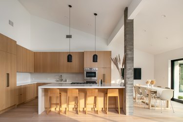 A kitchen filled with wood cabinets, a concrete pillar, and a white dining room table with white chairs.