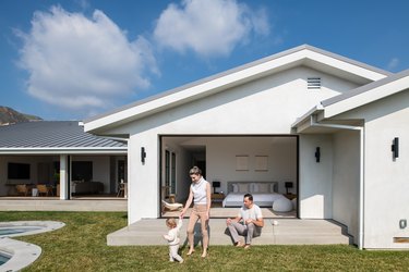 The family of three playing outside a white bedroom with a large open door.