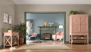 A room with pink tables and a cabinet looking to a room with a blue wall and green fireplace