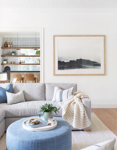 Light gray couch and blue ottoman against light hardwood floors