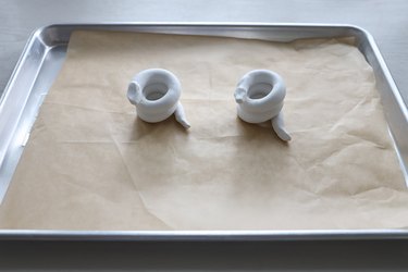 Two coiled snake clay candleholders on parchment lined baking tray