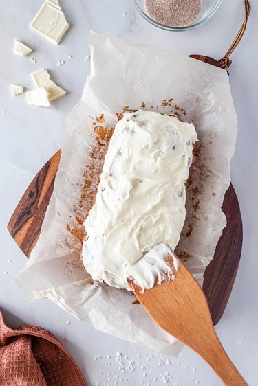 A wooden spatula spreading cream cheese frosting onto the pumpkin spice loaf