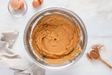 A metal bowl filled with a brown-orange mixture of the wet and dry ingredients.