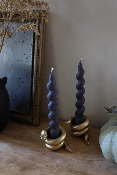 DIY gold snake candleholders with black spiral taper candles on table with pumpkin and mirror