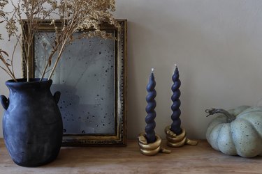 DIY gold snake candleholders with black spiral taper candles on table with pumpkin, mirror, and vase