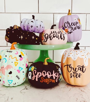A set of seven painted pumpkins in different shapes and colors. Some have stars, moons, baths, and random shapes on them. Others have phrases like "creep it real" or "let's go ghouls."