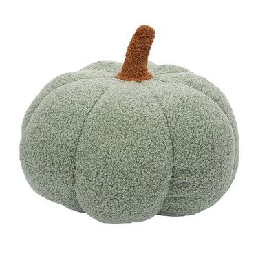 A plush sage green pumpkin pillow with a brown stem over a white background.