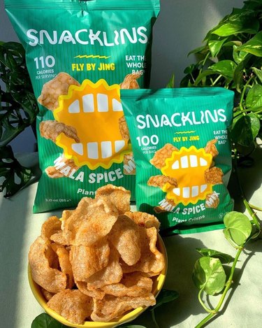 Snacklins Mala Spice Mix chips in a large bag and small, along with an overflowing bowl.