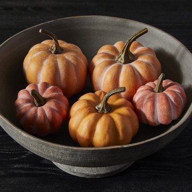 A rustic black fruit bowl filled with small pumpkins in varying shades of light and dark orange.