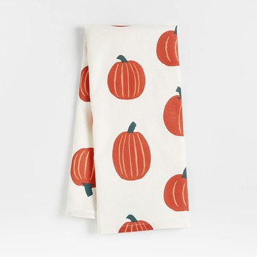 A white dish towel covered in tall and short orange pumpkin drawings with green stems.