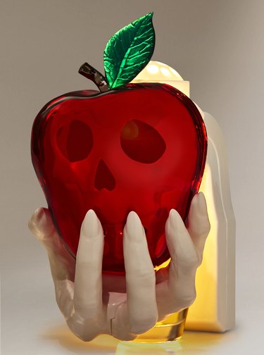 A nightlight in the shape of a white hand holding a poison apple. The apple is red with a brown stem and shiny green leaf. A skull can be seen in the apple.