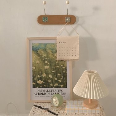 small tableau featuring wall hooks, calendar, framed art, alarm clock, and lamp