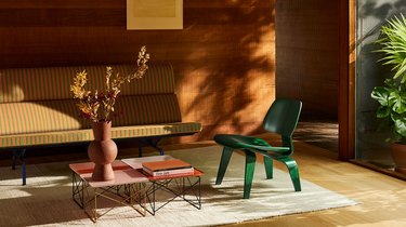 An emerald green wood Eames chair in a living room with an Eames sofa and four small side tables pushed together.