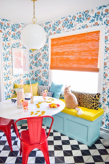 Dining nook with light blue booth, orange speckled wall paper and bright orange shade.