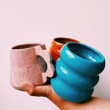 hand holding three colorful mugs