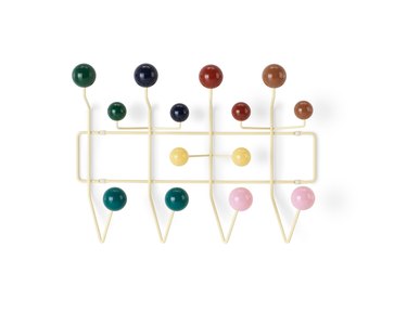 A wall coat hanger with colorful balls on the end of each hook.