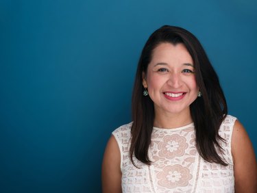 person with long black hair and white shirt against a teal background