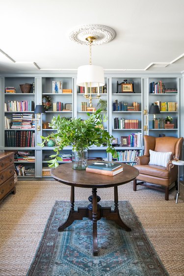 Library with light blue bookshelf, hanging chandelier, and dark furniture.