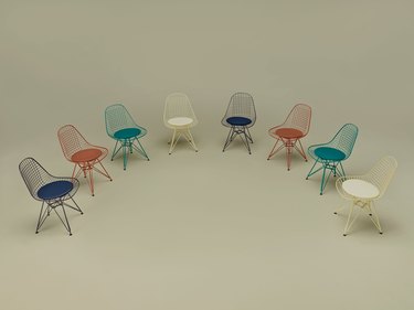Eames wire chairs in cream, teal, burnt orange, and navy facing each other in a half circle.